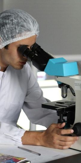 a man using a microscope, wearing laboratory gear