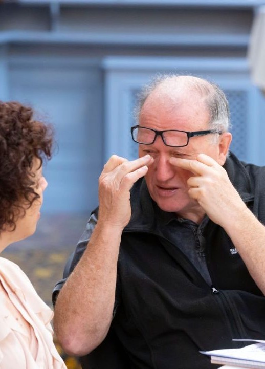 A man with his hands close to his eyes and glasses hanging on his forehead whilst speaking with a women